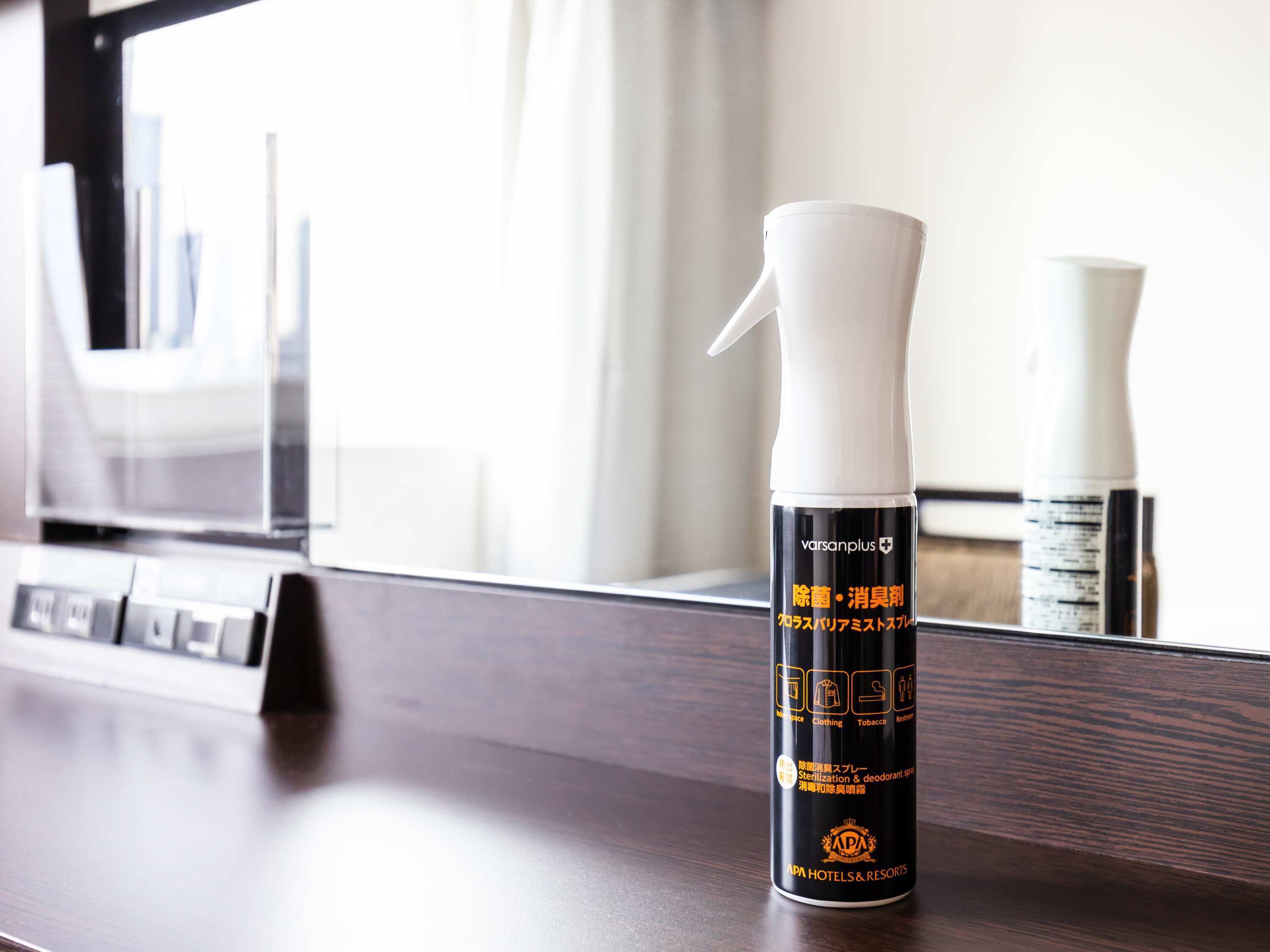 A hotel room with a minibar, a mirror, and a spray bottle on the counter.