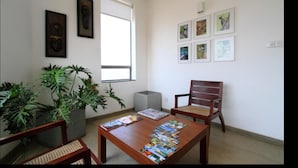 A room with a wooden table, two chairs, a potted plant, and framed pictures on the walls. - The Ocean Front (Colombo)