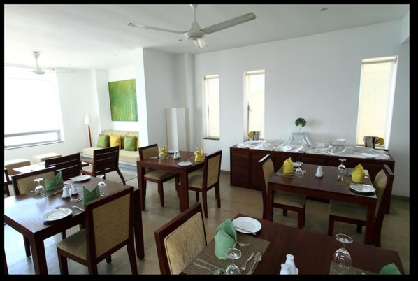 Un espace repas avec plusieurs tables dressées pour les repas, un ventilateur de plafond et de grandes fenêtres laissant entrer la lumière naturelle.