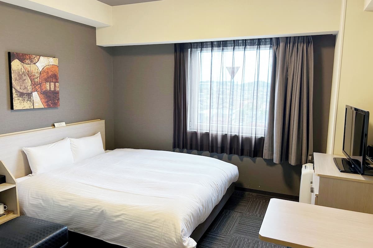 A hotel room with a large bed, a desk, a television, and a window with curtains.