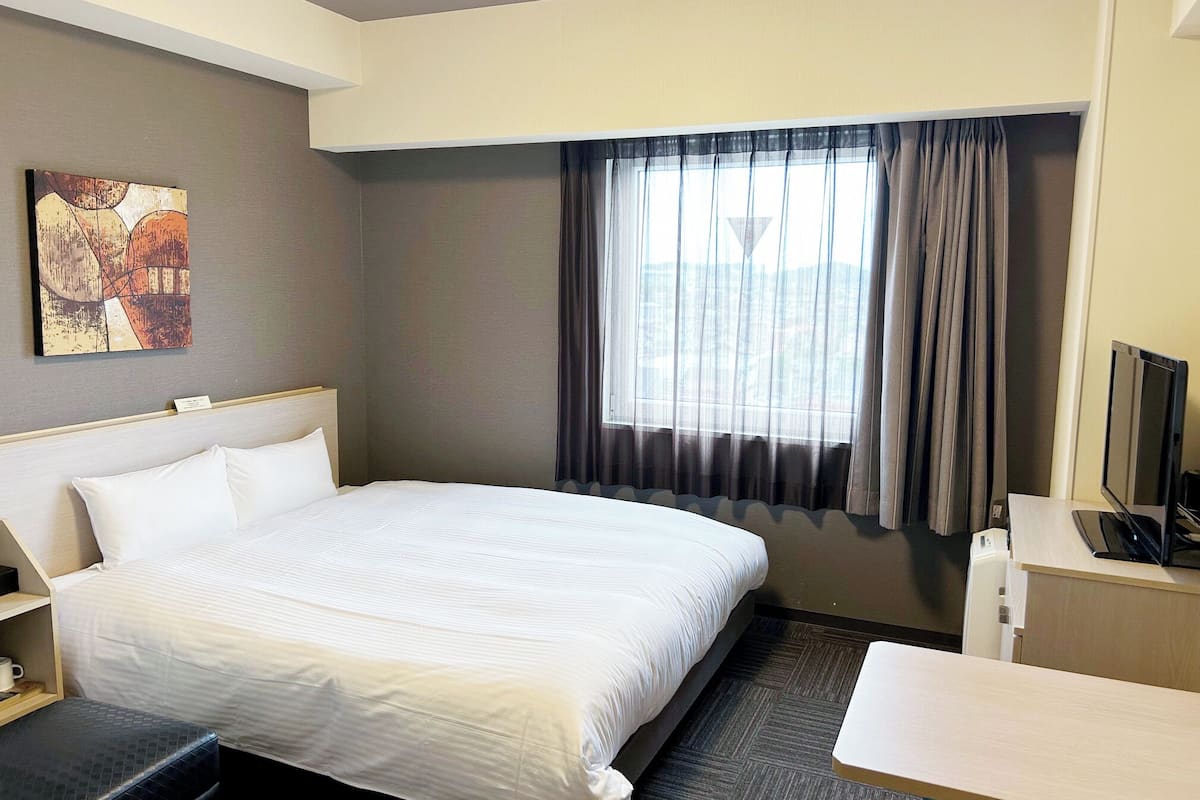 A hotel room with a bed, a desk, a television, and a window with curtains.