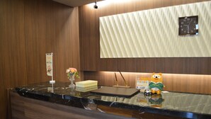 Un mostrador de recepción de hotel con pared de paneles de madera, un reloj, un florero con flores y una figura de un oso.