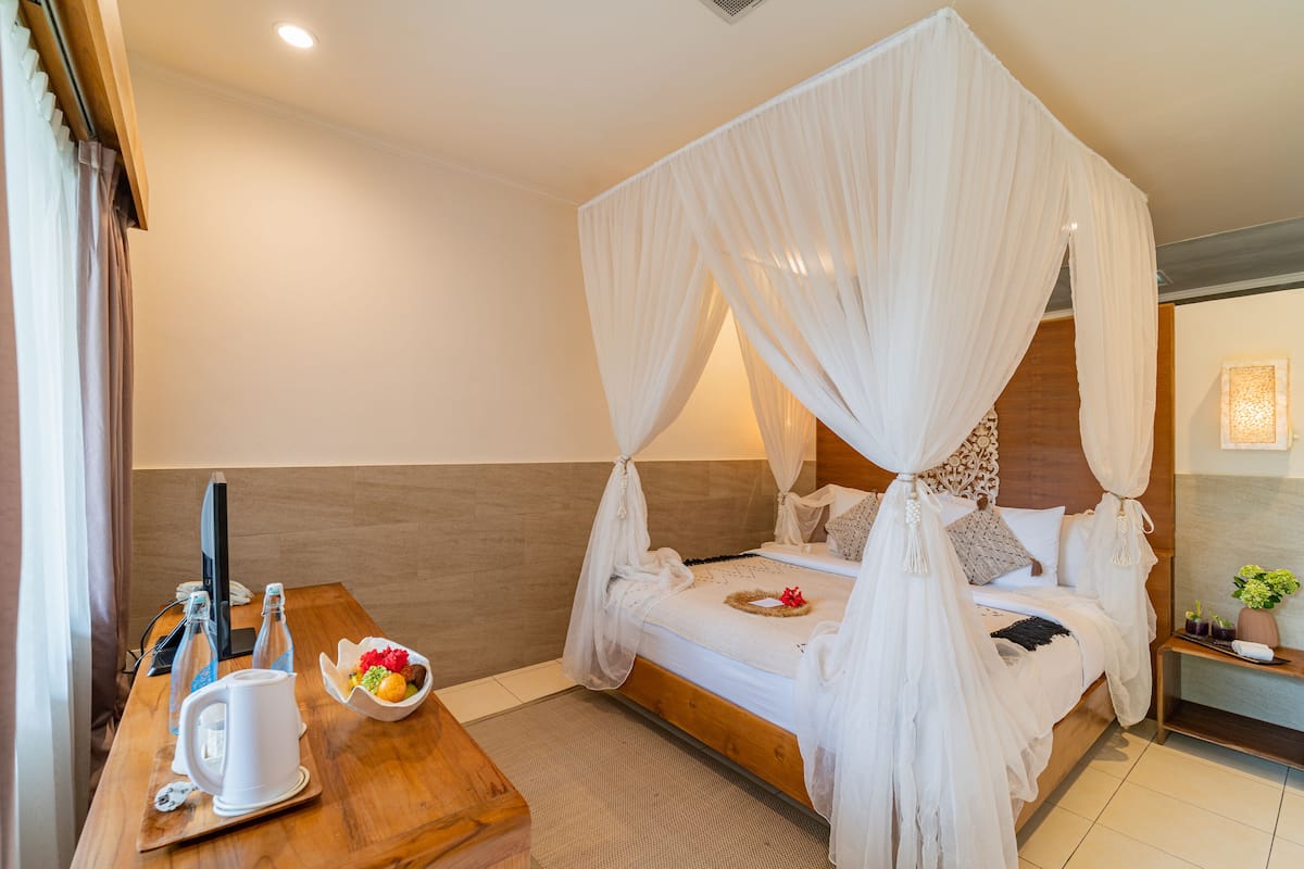 A bedroom with a four-poster canopy bed, a wooden bedside table with a kettle, a bowl of fruit, and a bedside phone.