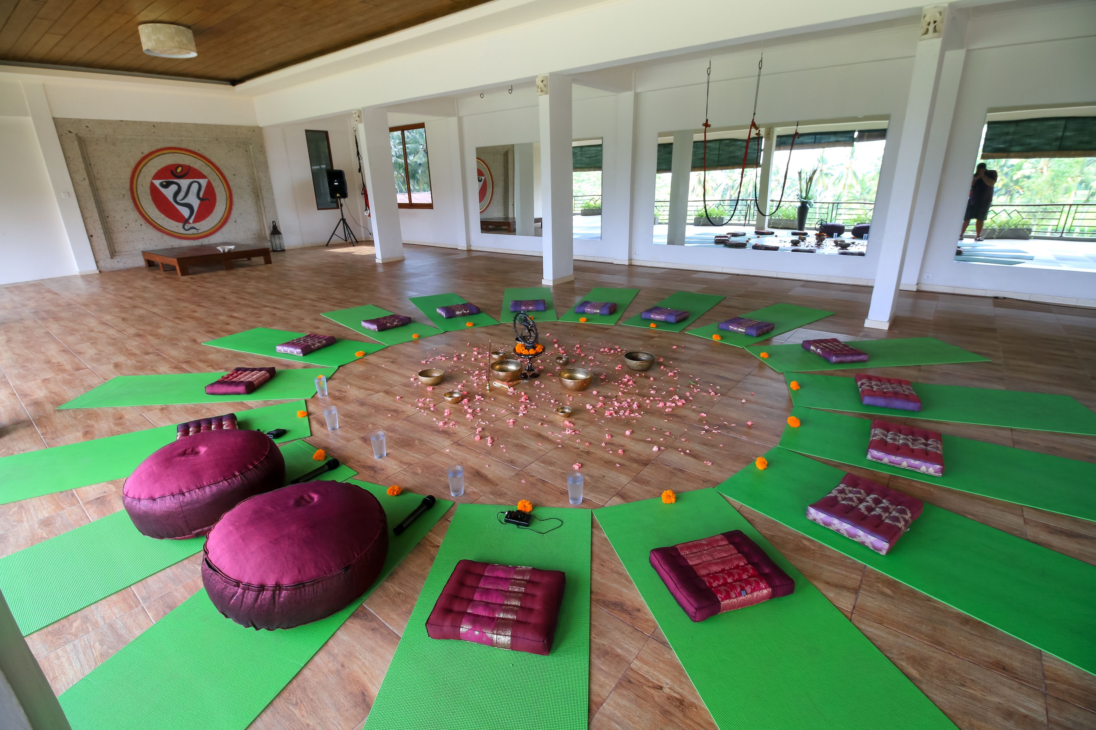 A spacious room with a circular arrangement of mats and cushions, a wooden floor, and a large wall with a circular design.