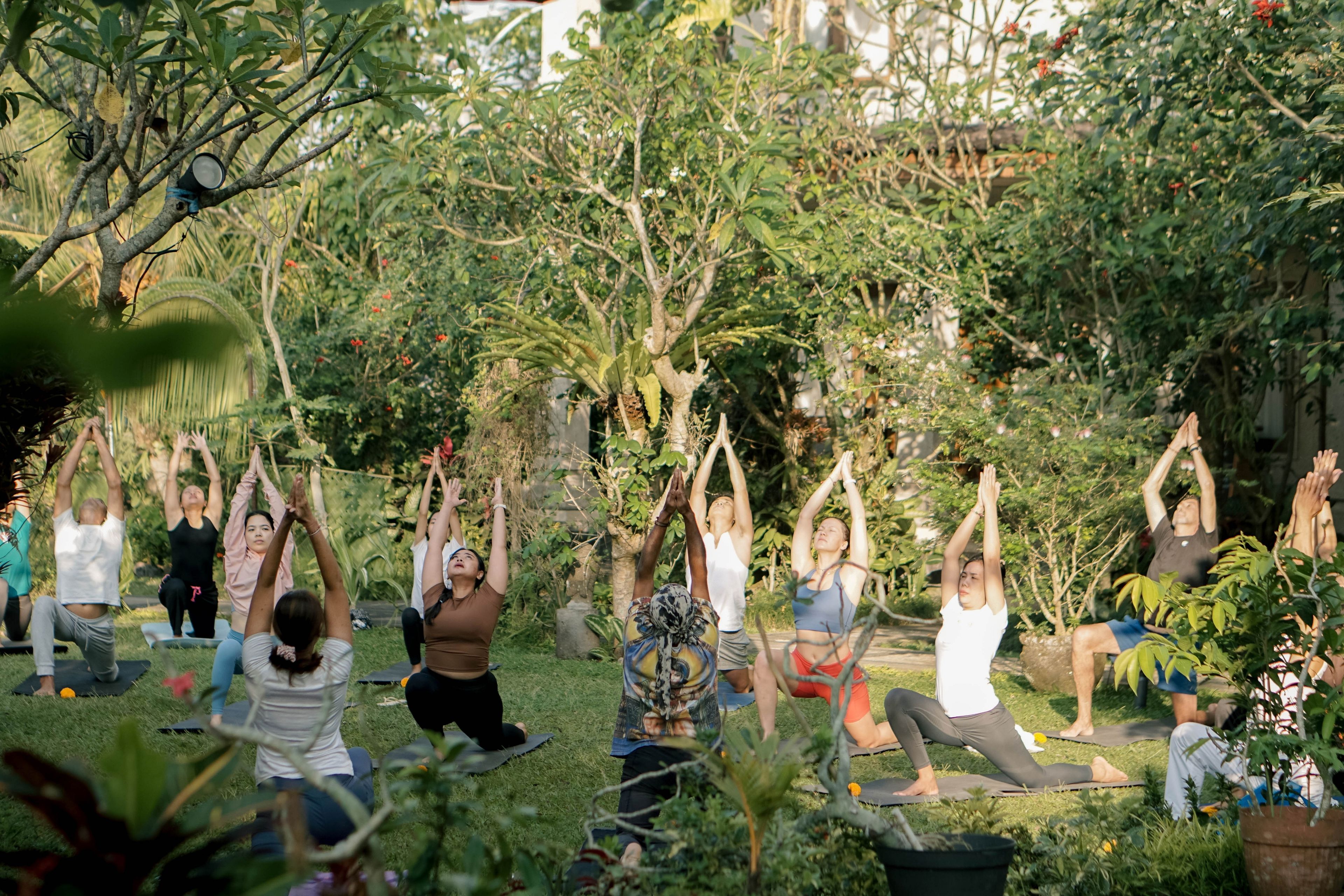 A group of people performing yoga outdoors in a garden setting.