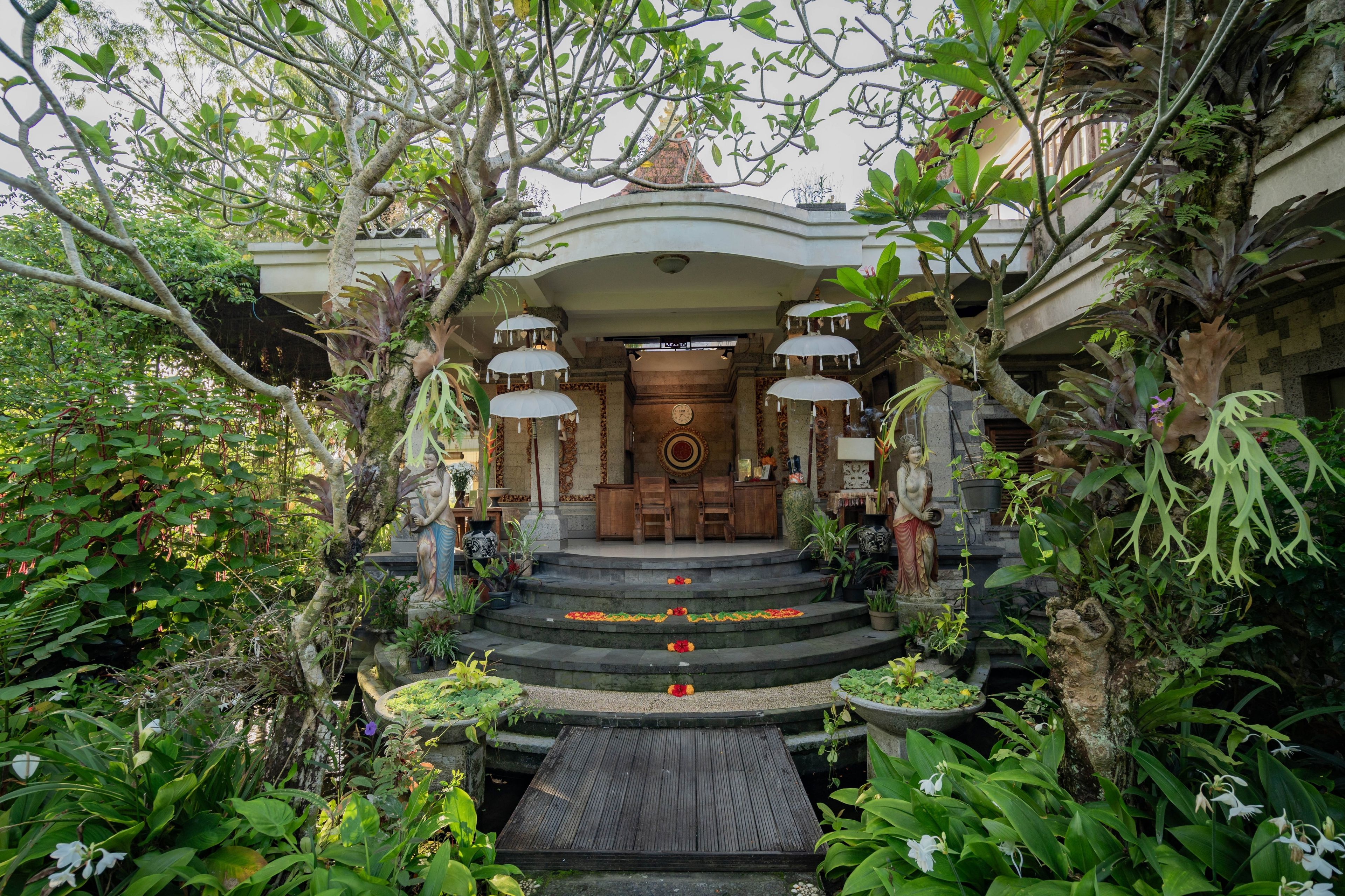 Un edificio tradicional con una entrada central, rodeado de abundante vegetación y estatuas.