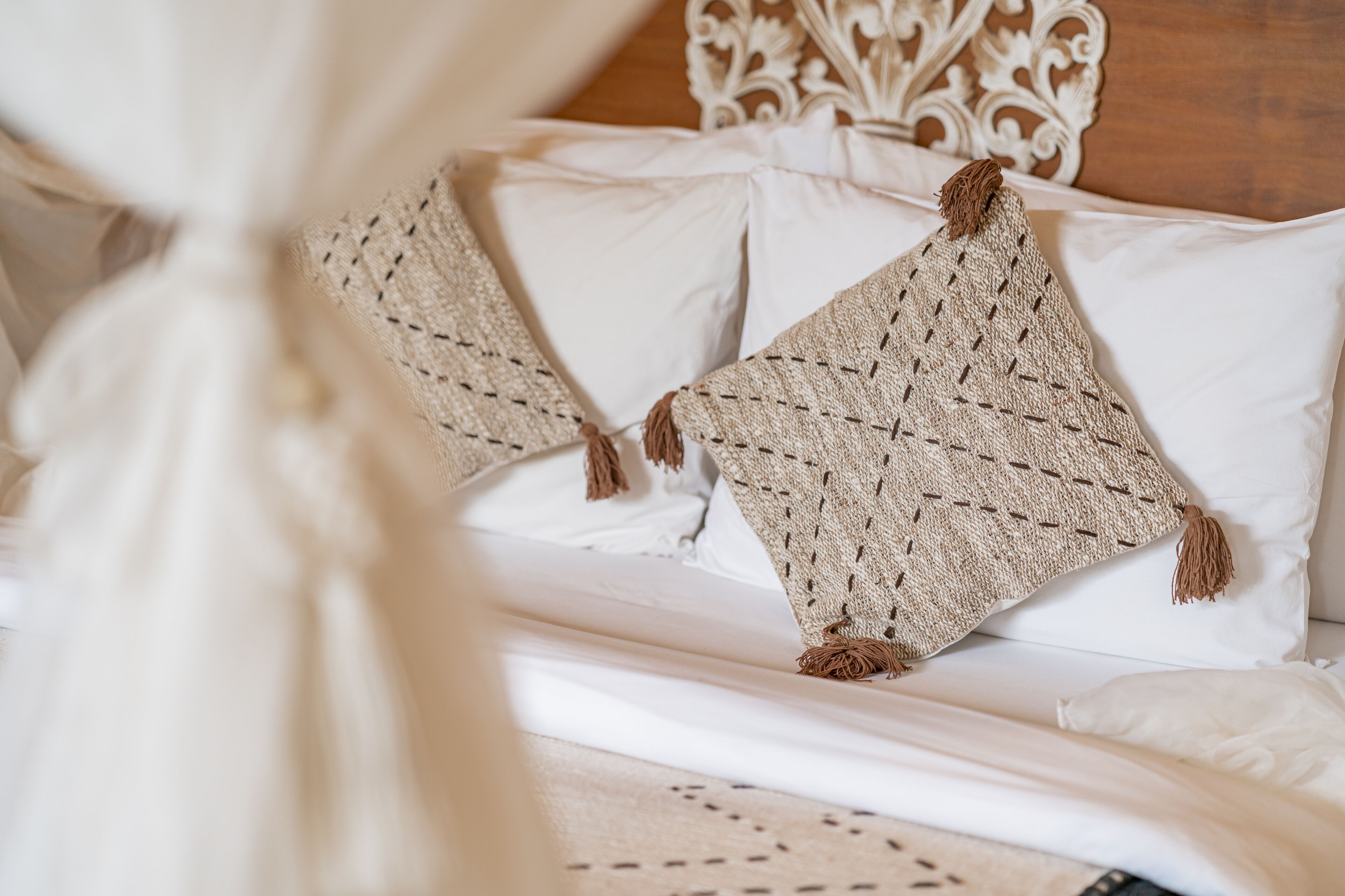 Una cama con cabecera blanca, dos almohadas y una colcha tejida con flecos.