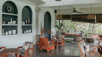 Una habitación amplia con techo alto, muebles de mimbre y diversos objetos decorativos en estanterías.