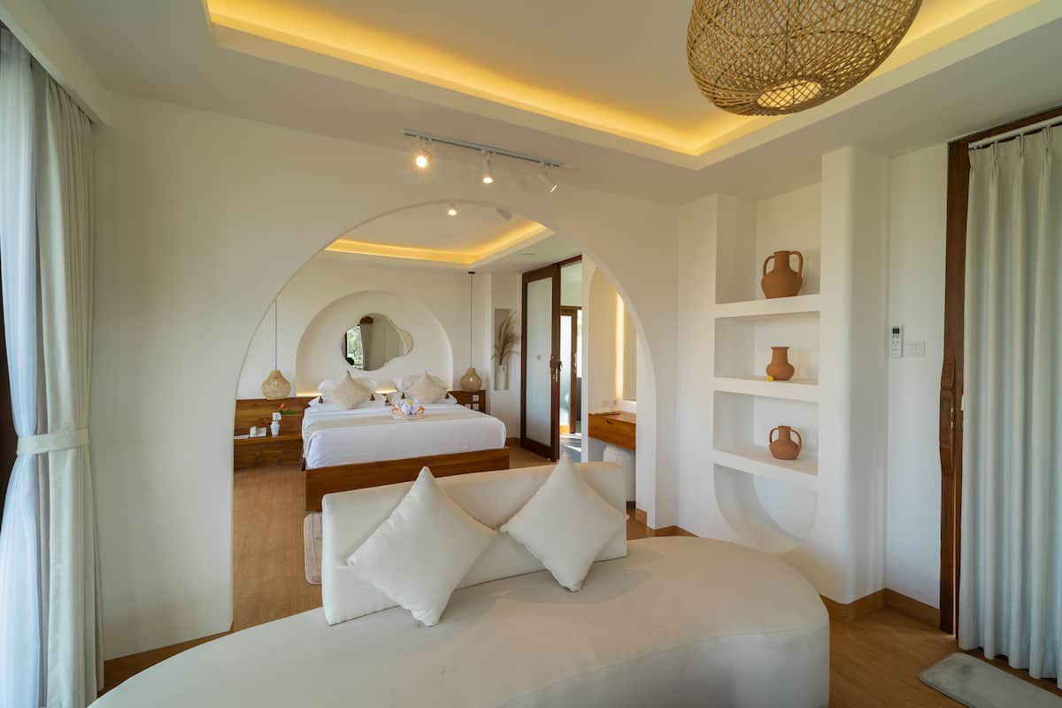 A modern hotel room with a large bed, a sofa, and a dining area.