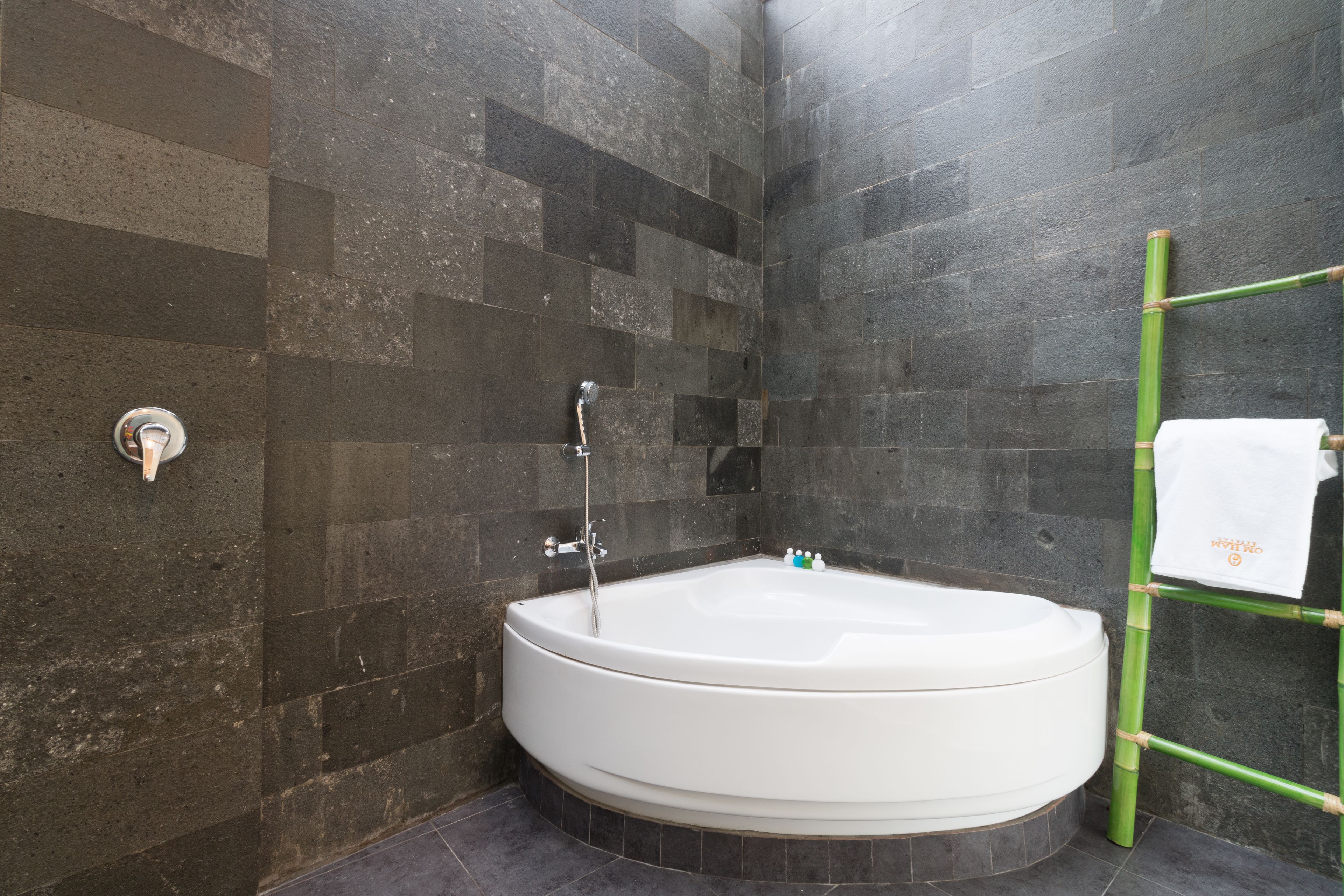 A modern bathroom with a freestanding bathtub, dark stone tiles, and a bamboo towel rack.