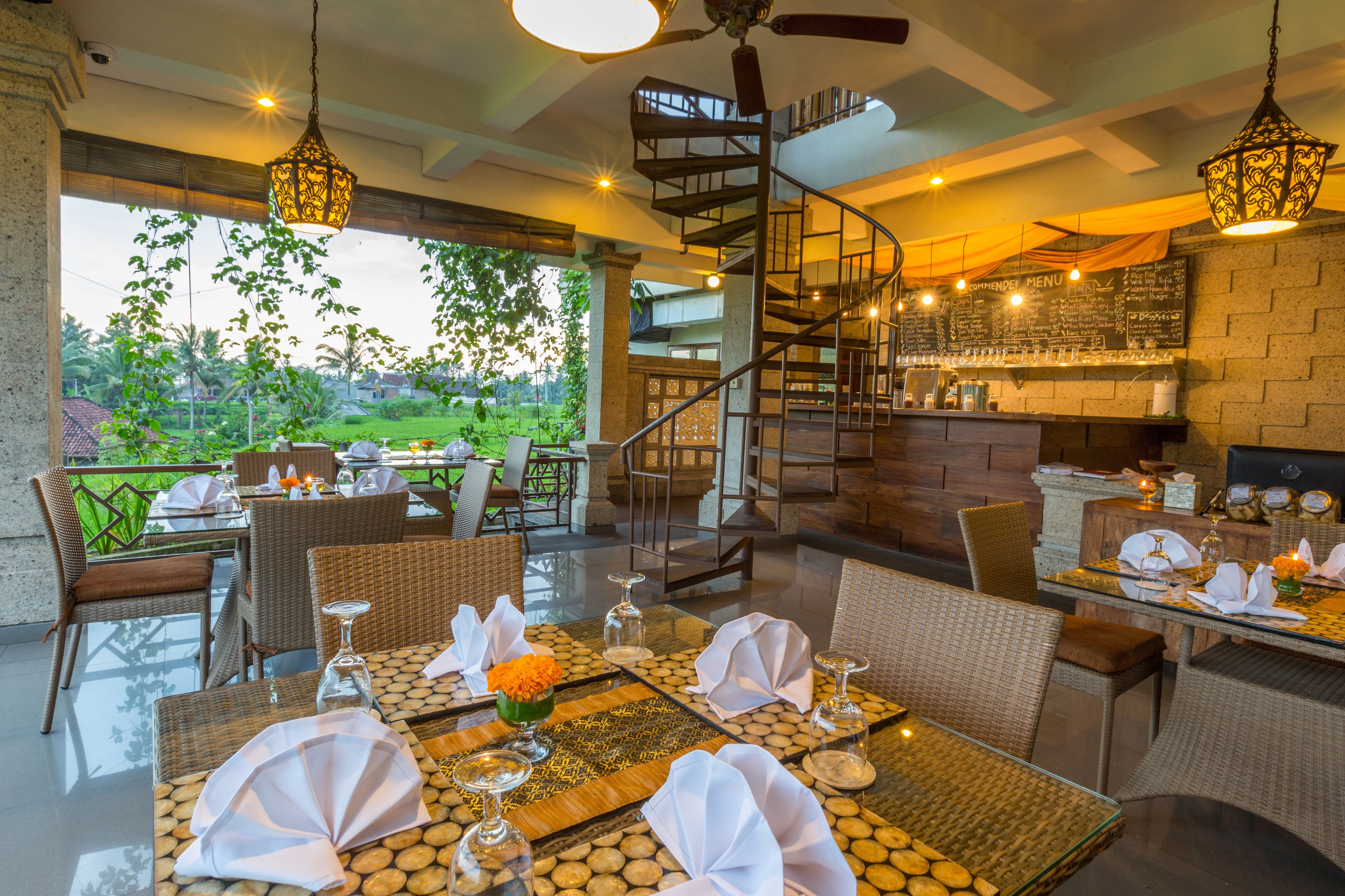 A restaurant with outdoor seating, a spiral staircase, and a view of greenery.