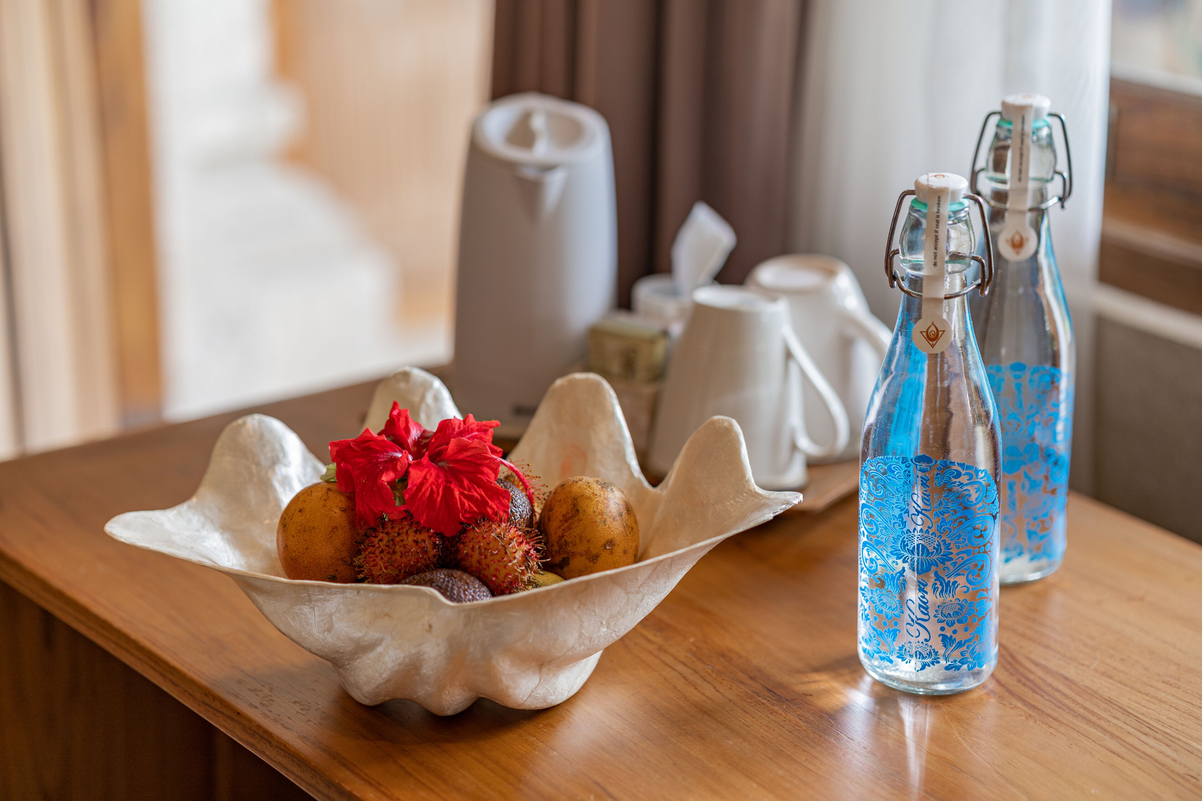 A wooden table with a decorative bowl containing fruits and two glass bottles with blue designs.