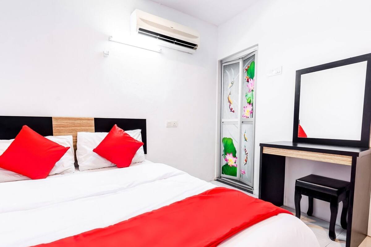Una habitación de hotel con cama, escritorio, silla, equipo de aire acondicionado y una puerta de vidrio decorativa.