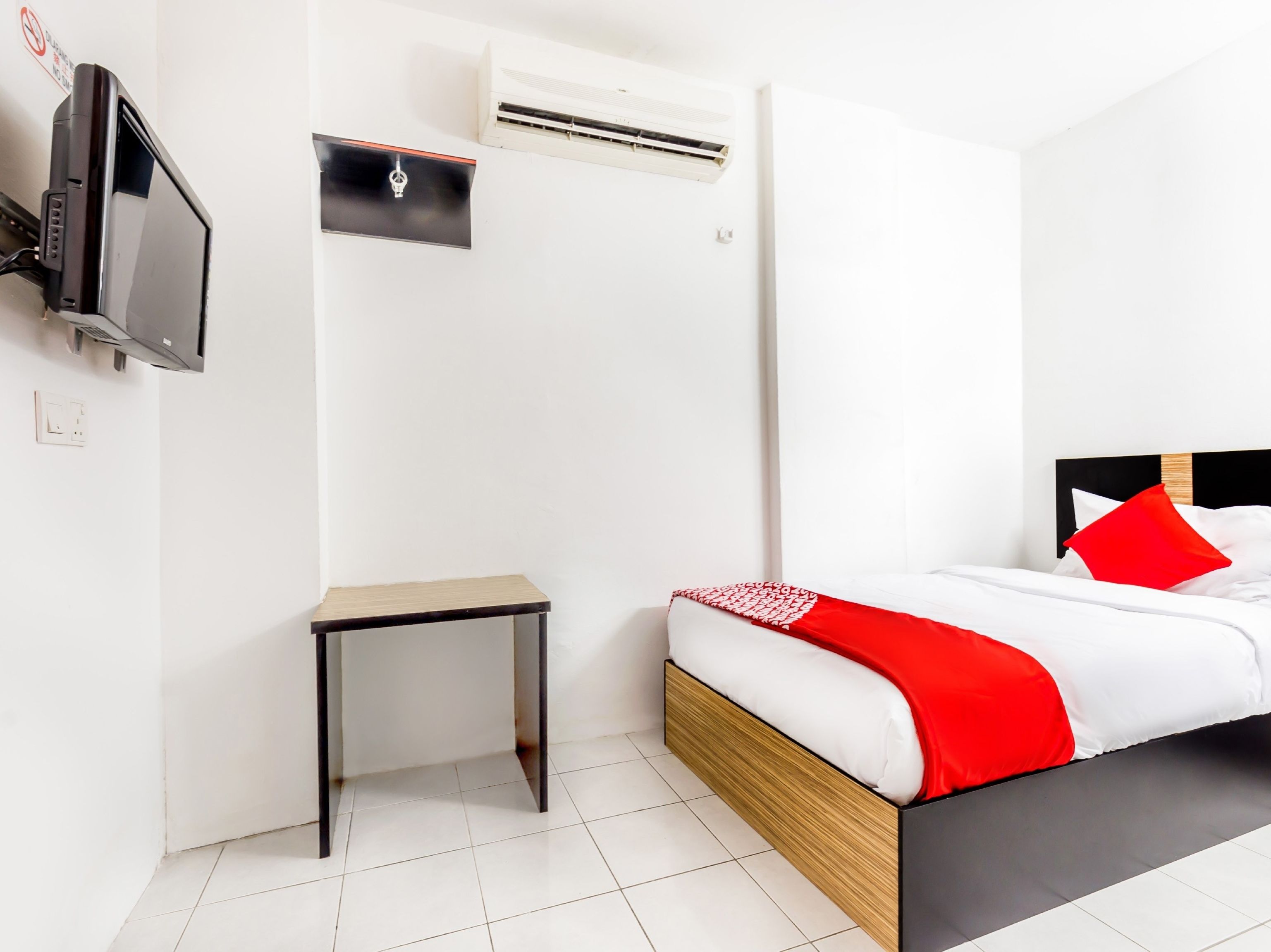 Una habitación de hotel con una cama, una mesita, un aire acondicionado y un televisor.