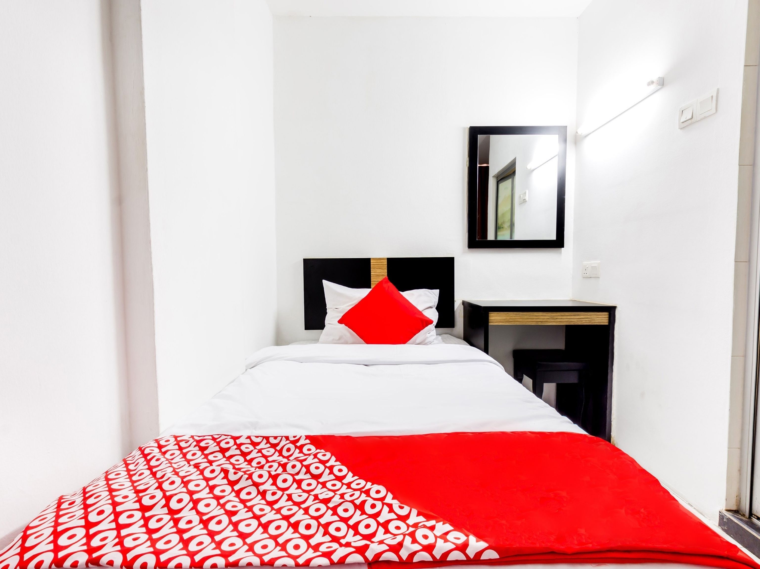 A narrow hotel room with a bed, a small desk, and a mirror on the wall.
