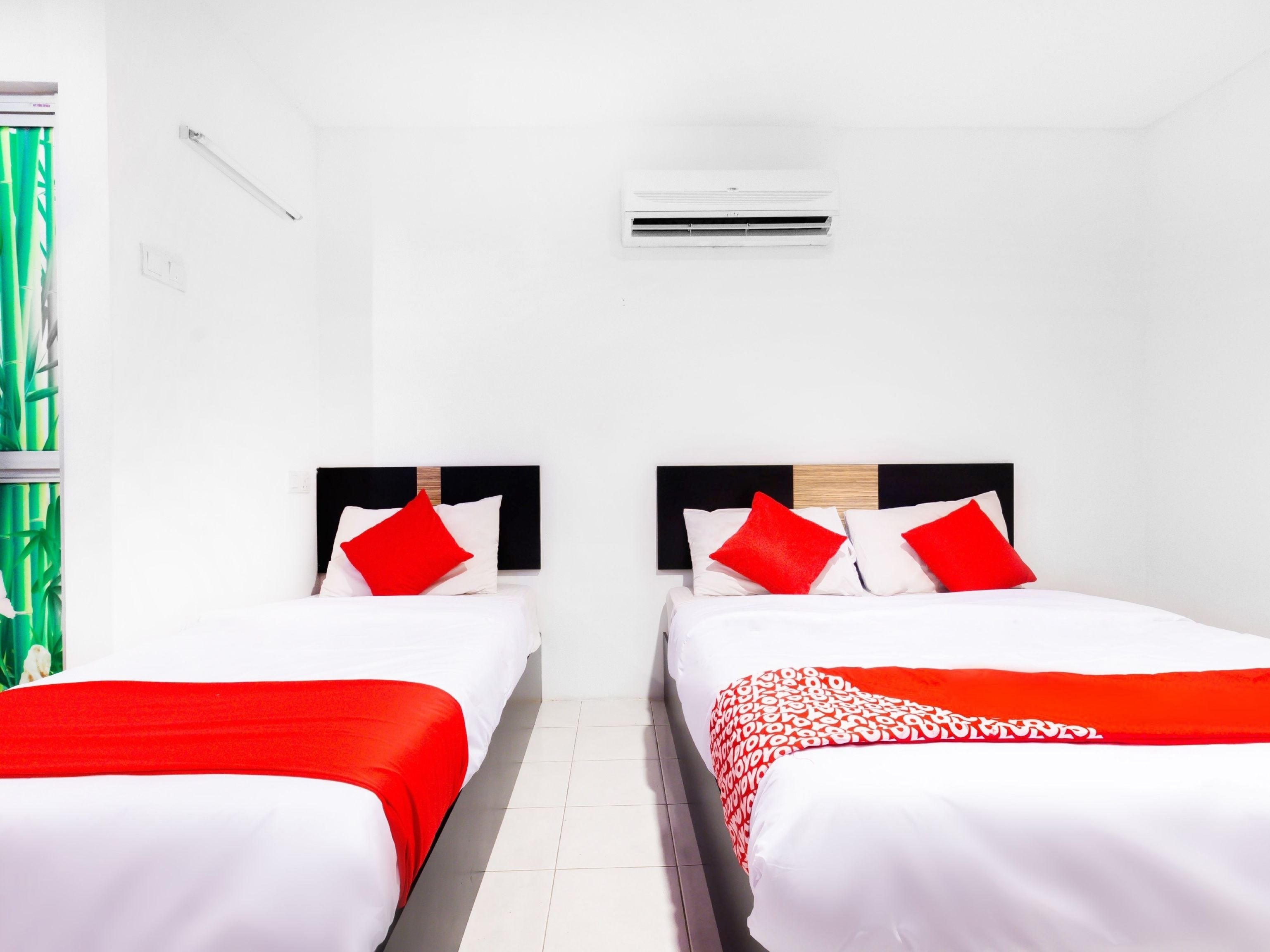Ein Hotelzimmer mit zwei Betten, jeweils mit roter und weißer Bettwäsche, einem Holzkopfstück und einer kleinen Klimaanlage an der Wand.