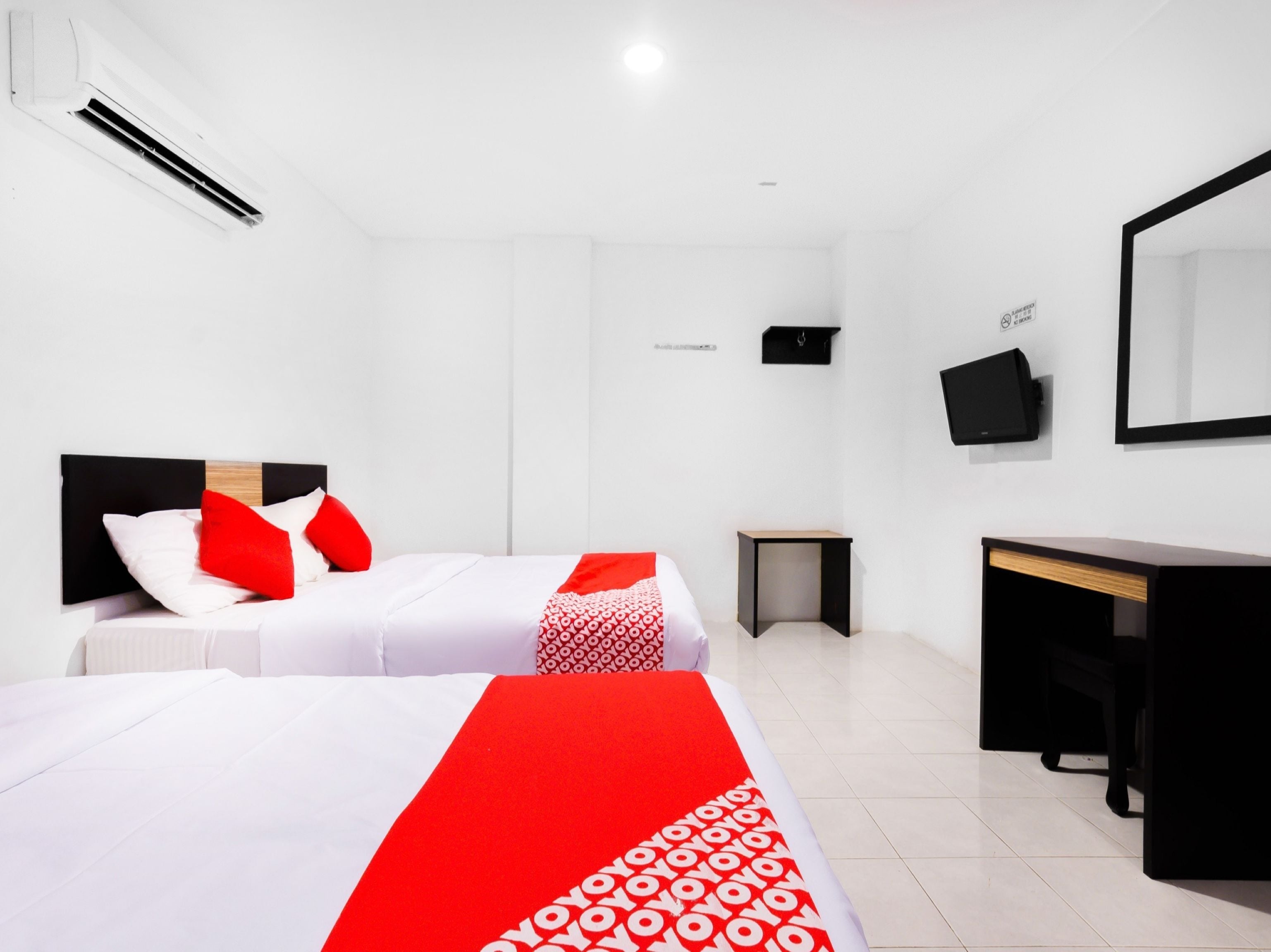 A hotel room with two beds, a desk, a chair, a small table, and a mirror.