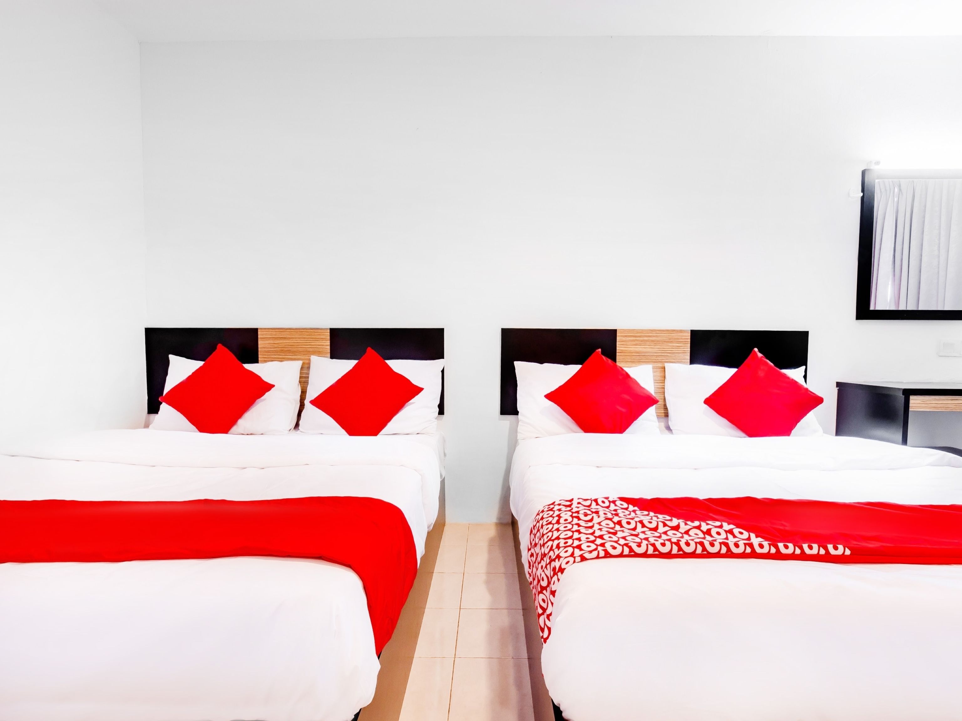 Two single beds with red and white bedding, a wooden headboard, and a white wall with a framed picture.