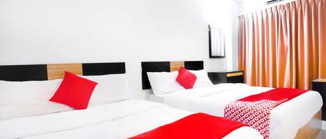 Ein Hotelzimmer mit zwei Betten, weißer Bettwäsche, roten Kissen und einer roten Decke mit Muster.