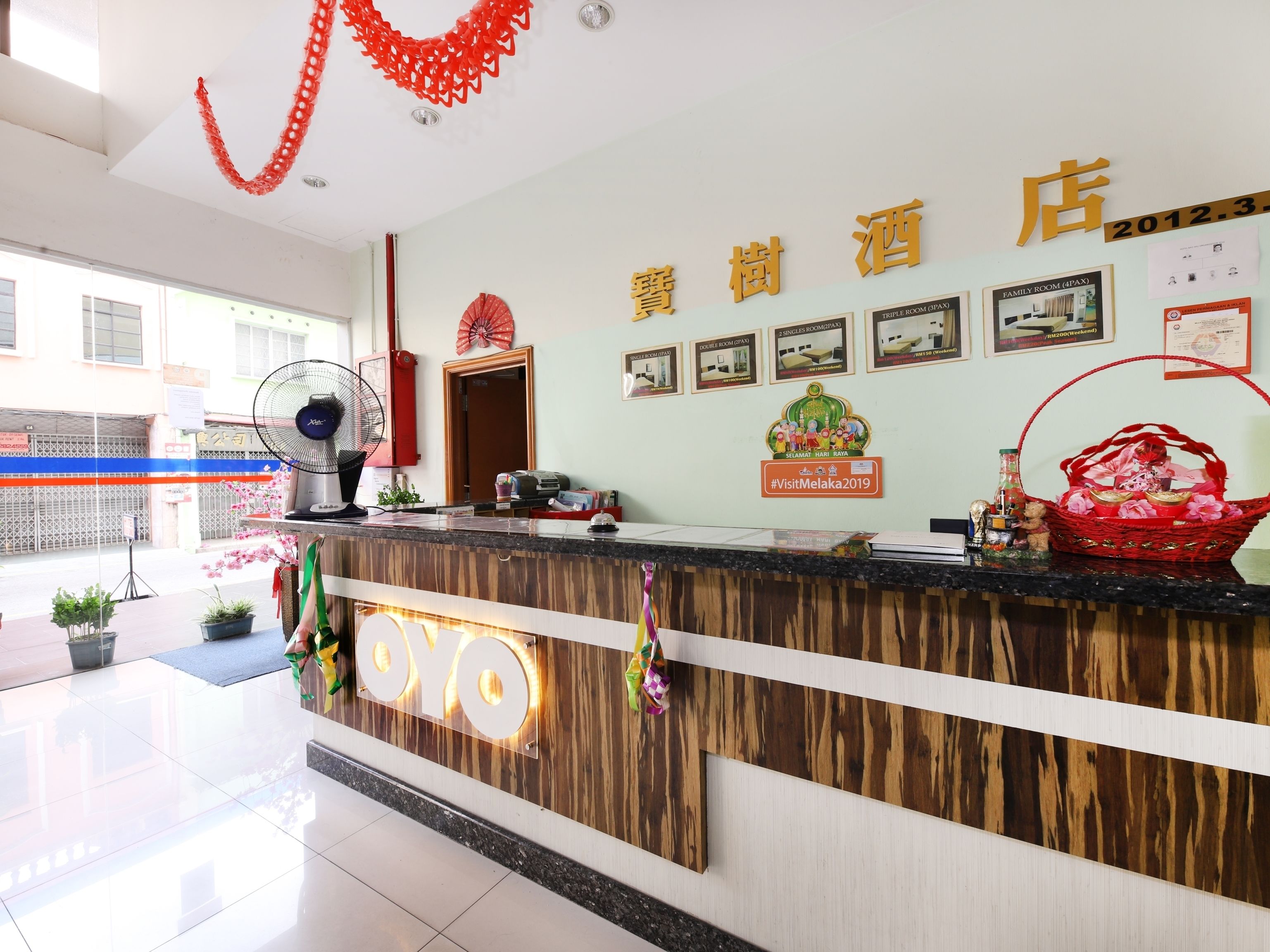A hotel reception desk with a wooden finish, a large fan, and a red decorative hanging.