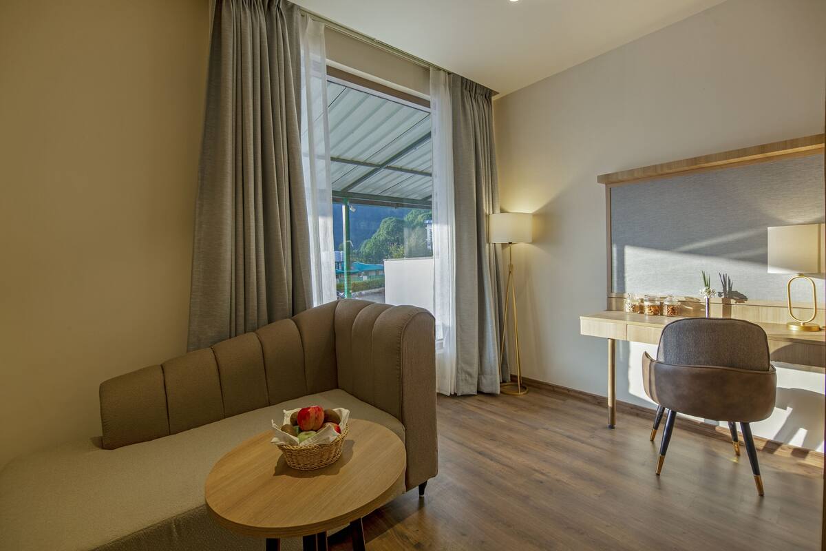 A modern room with a sofa, a small round table with a fruit basket, a desk with a lamp, and a chair.