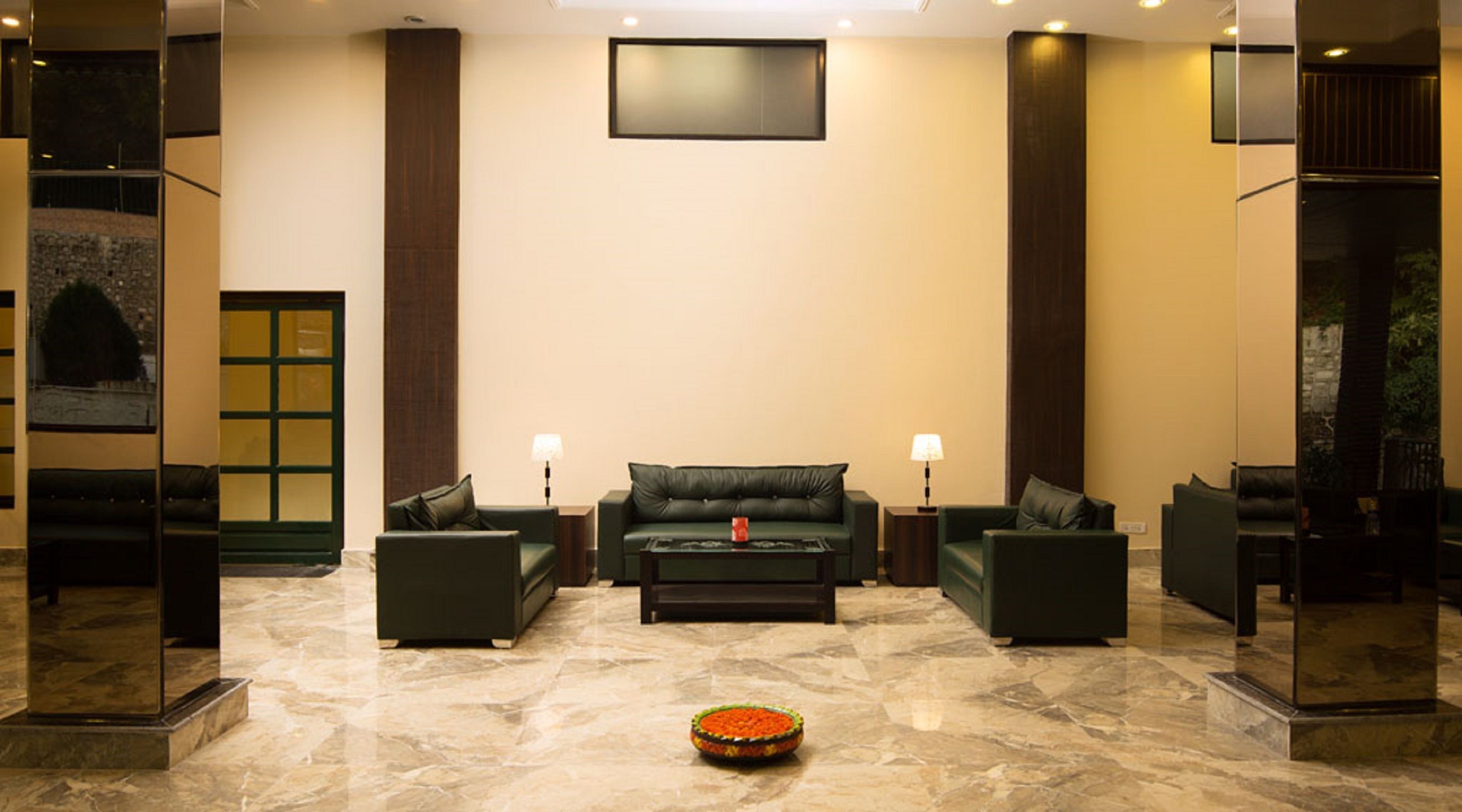 A lobby with a green sofa set, two side tables with lamps, a coffee table, and a decorative bowl on the floor.