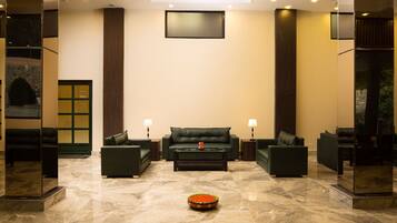 A lobby with a green sofa set, two side tables with lamps, a coffee table, and a decorative bowl on the floor.