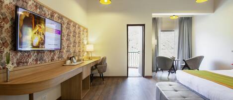 A hotel room with a wooden desk, a bed, a sofa, and a television mounted on the wall.
