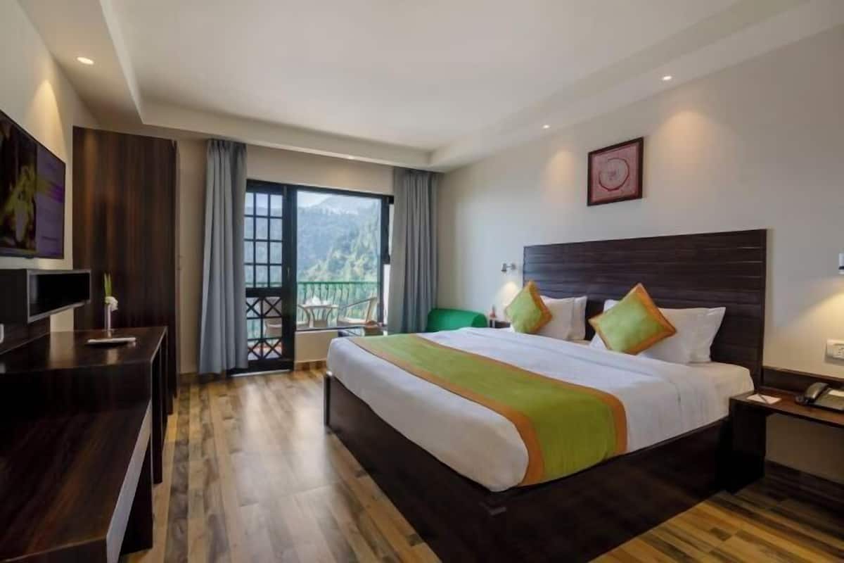 A hotel room with a large bed, a desk, a chair, a TV, and a balcony with a view.