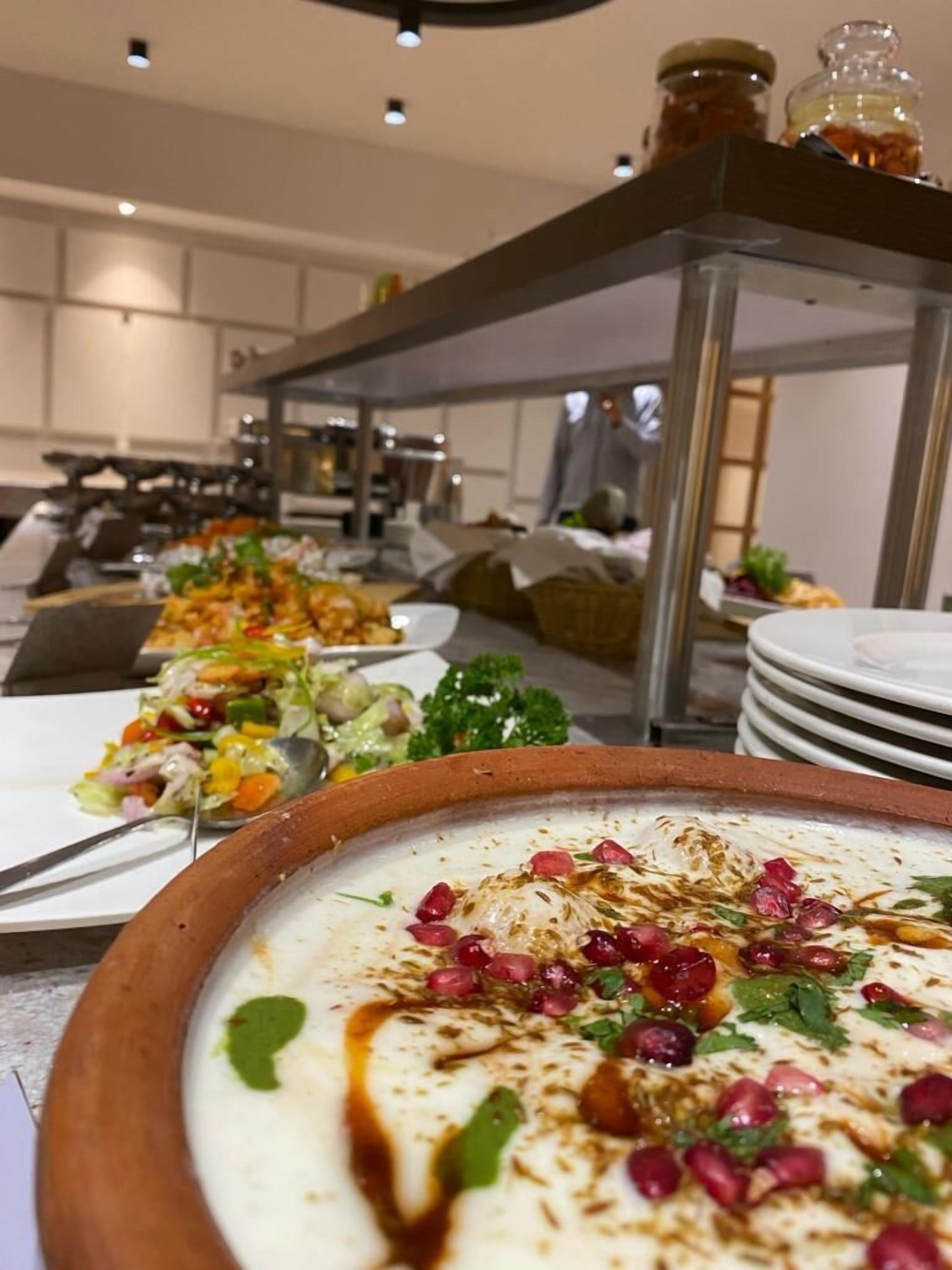 Montaje de bufé con diversos platos, incluyendo un tazón de comida cremosa decorada con hierbas y semillas de granada.