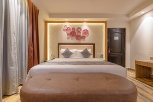Habitación de hotel con una cama grande, cabecera de madera, panel decorativo en la pared, mesita de noche con una botella y una puerta con un letrero.