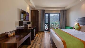 Habitación de hotel con cama, escritorio, televisión y balcón con vistas a las montañas.