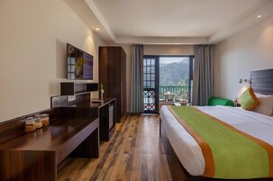 Habitación de hotel con cama, escritorio, televisión y balcón con vistas a las montañas.