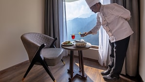 A chef serving a meal at a table by a window with a view of mountains. - Sterling Nainital (Nainital)