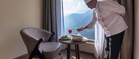 A chef serving a meal at a table by a window with a view of mountains.