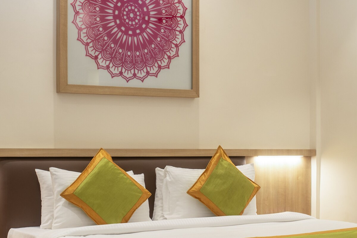 Una cama bien hecha con ropa de cama blanca y detalles verdes, una obra de arte con mandala enmarcada en la pared y un cabecero de madera.