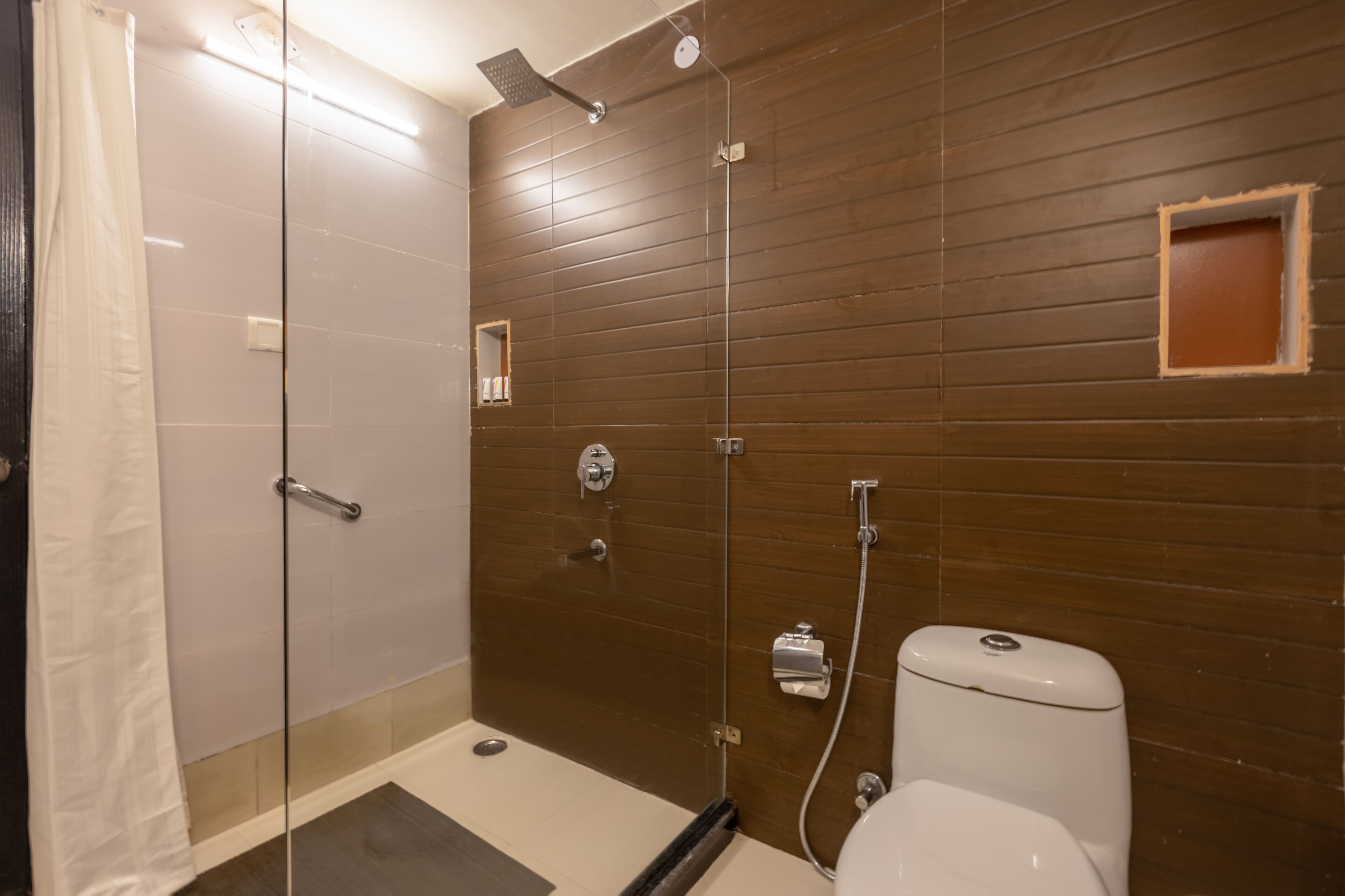 A modern bathroom with a glass shower enclosure, a toilet, and a small mirror.