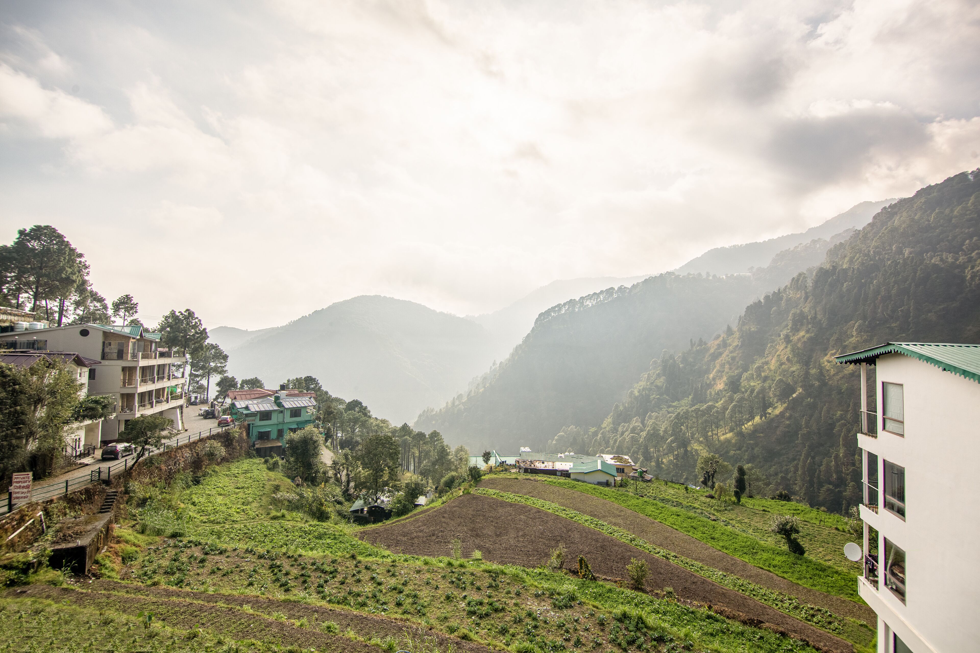 A hillside village with terraced fields, buildings with balconies, and a mountainous backdrop.