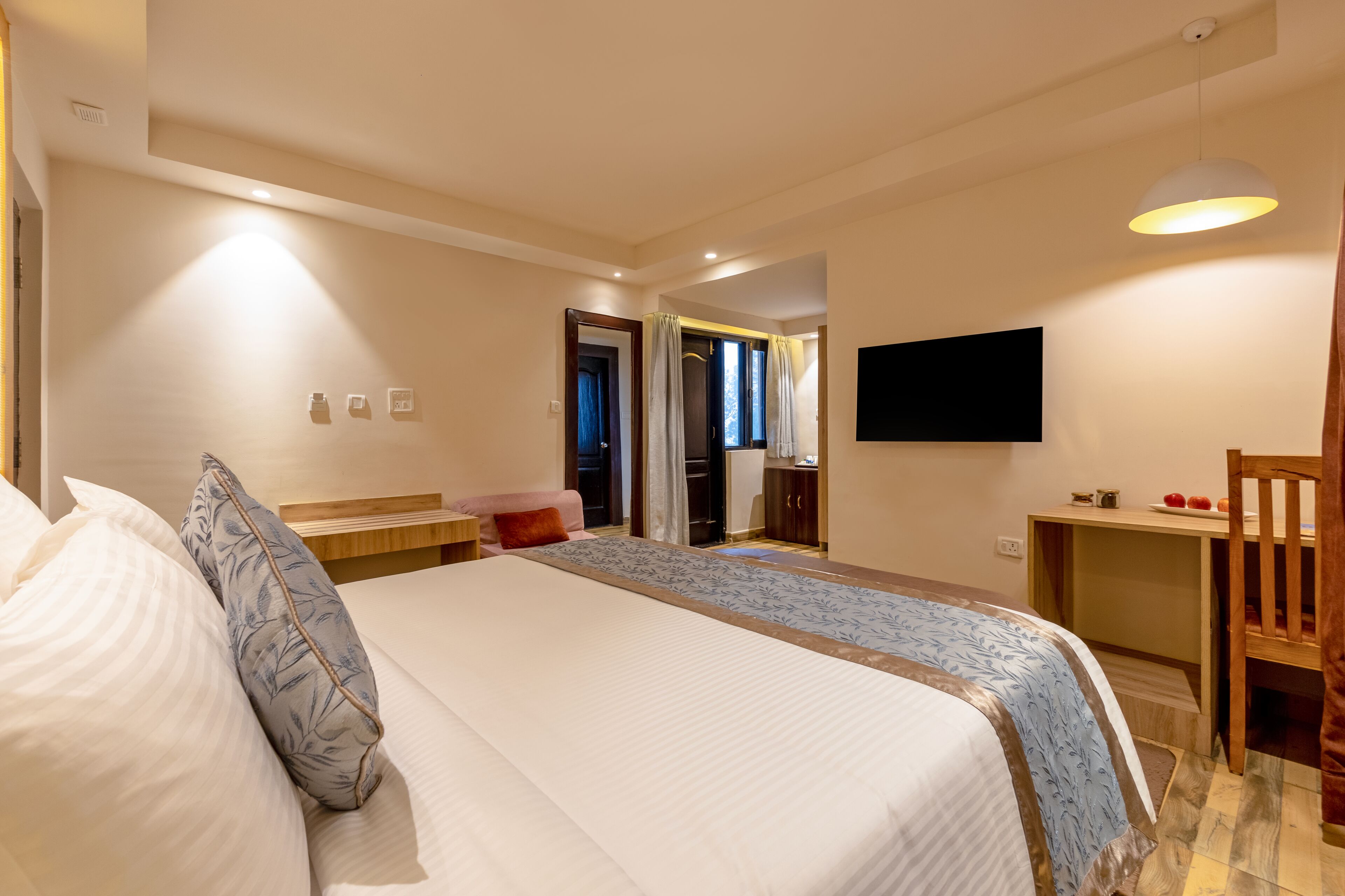 A hotel room with a bed, bedside table, TV, and a view of the outside.