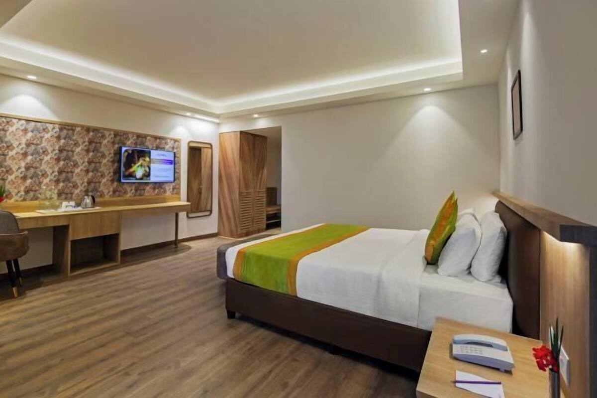 A hotel room with a bed, desk, TV, and a wooden floor.