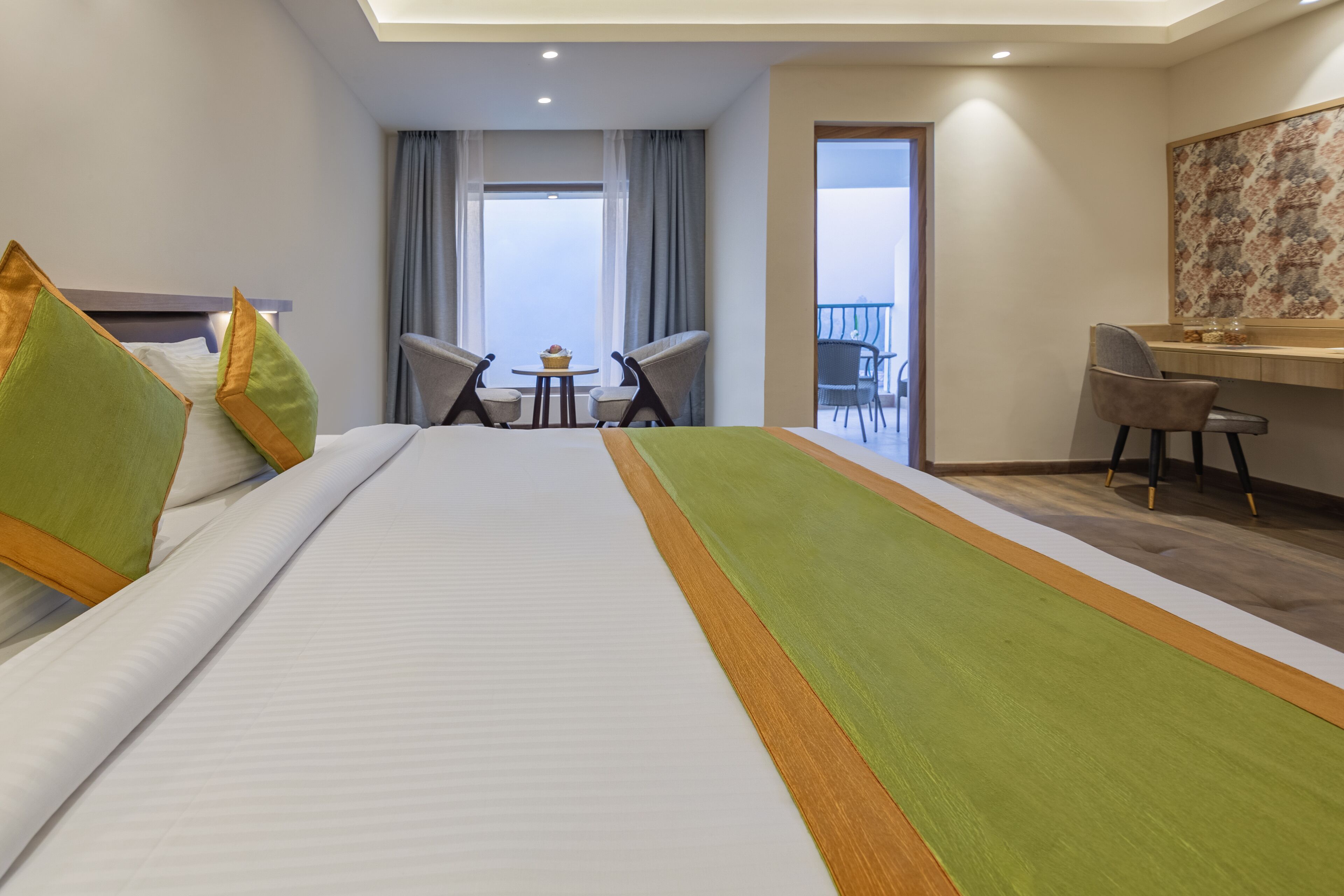 Habitación de hotel con una cama grande, un escritorio, dos sillas, una mesita con un cupcake y un balcón con vistas.