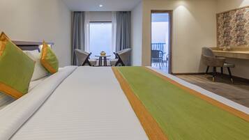 Habitación de hotel con una cama grande, un escritorio, dos sillas, una mesita con un cupcake y un balcón con vistas.