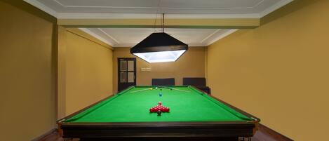 A pool table with a green felt surface, surrounded by wooden flooring and beige walls.