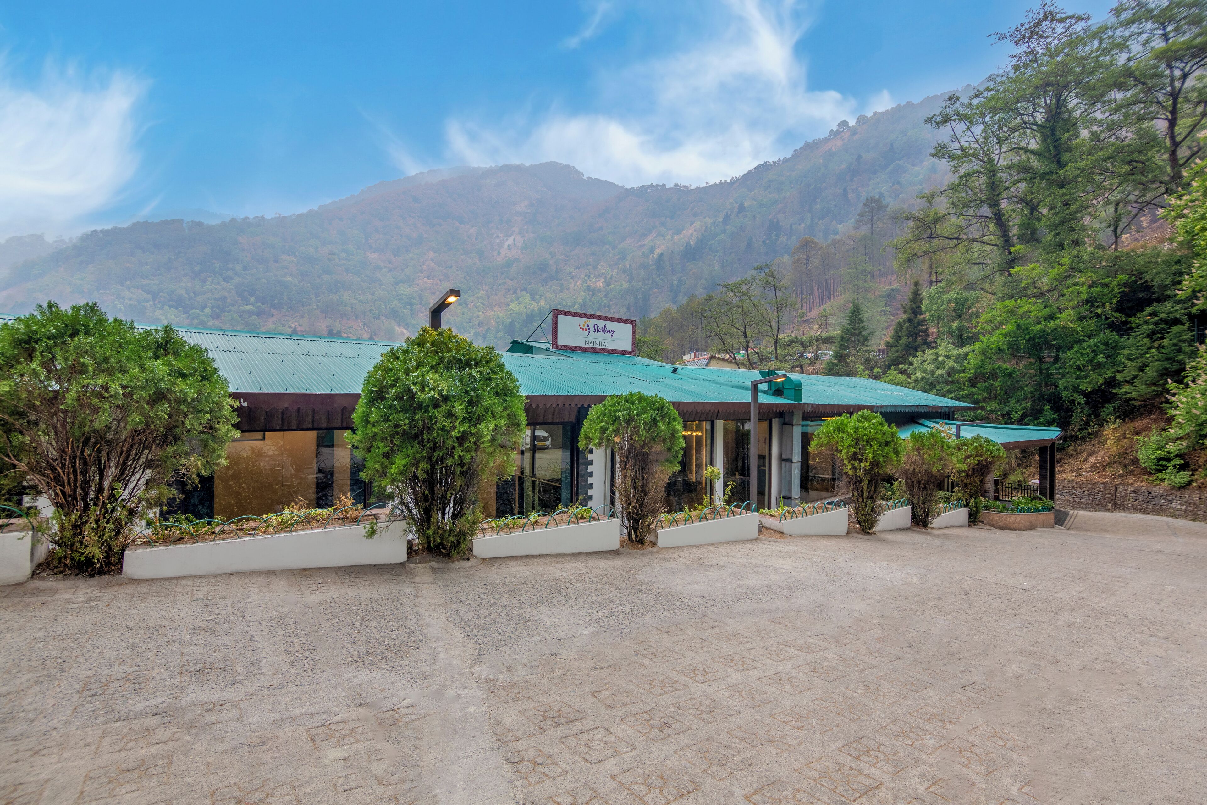 A hotel with a green roof, surrounded by trees and mountains.