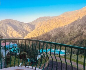 Paisaje montañoso con vista a un edificio de techo verde y barandilla de balcón.