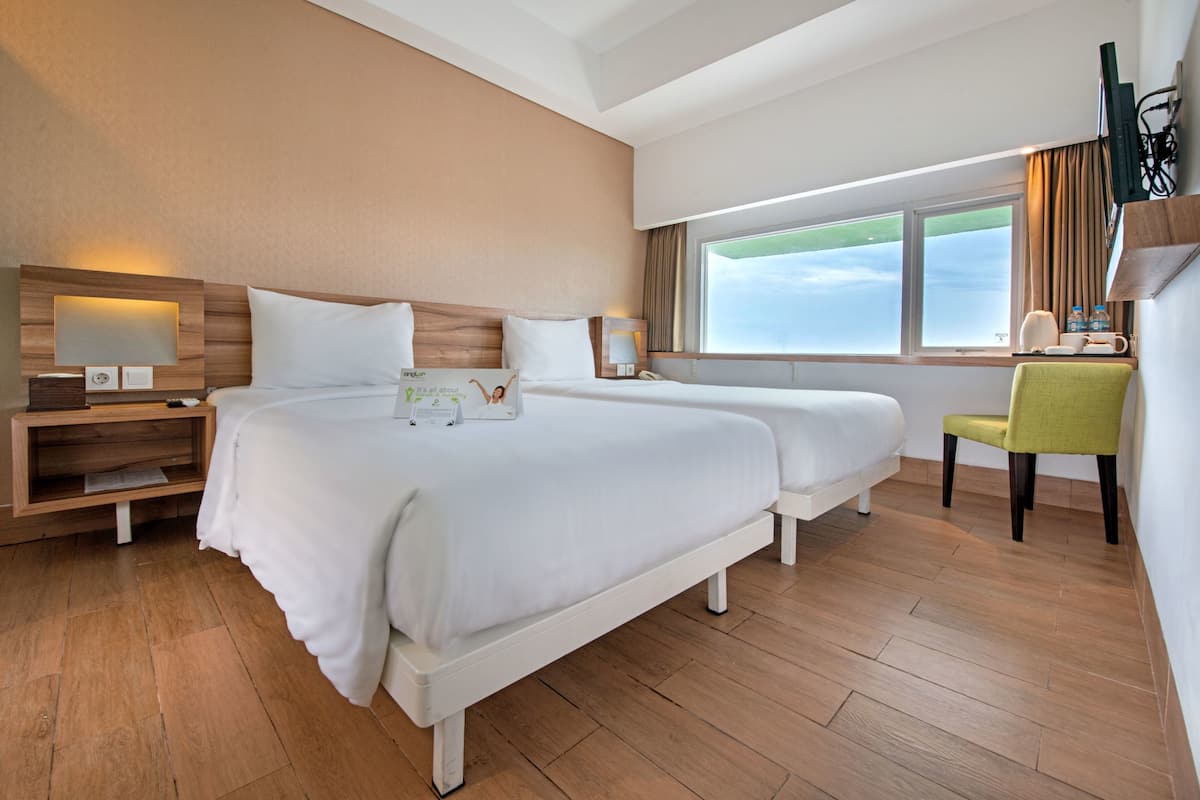 A hotel room with two beds, a desk, a chair, a TV, and a window with a view.