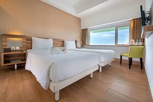 Habitación de hotel con dos camas, un escritorio, una silla, un televisor y una ventana con vistas.