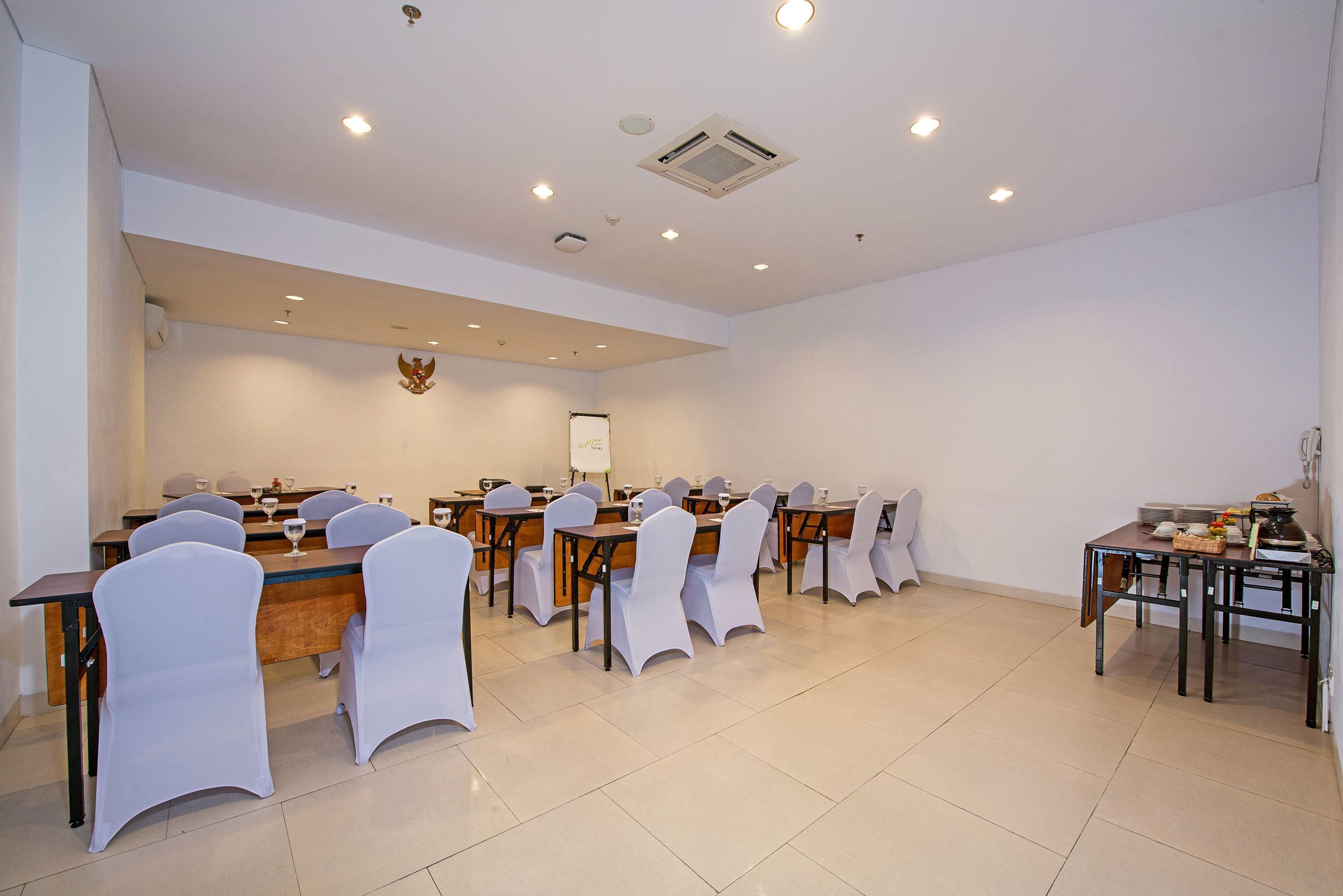 Ein Konferenzraum mit mehreren Tischen und Stühlen, weißen Stuhlhussen und einer Tafel an der Wand.