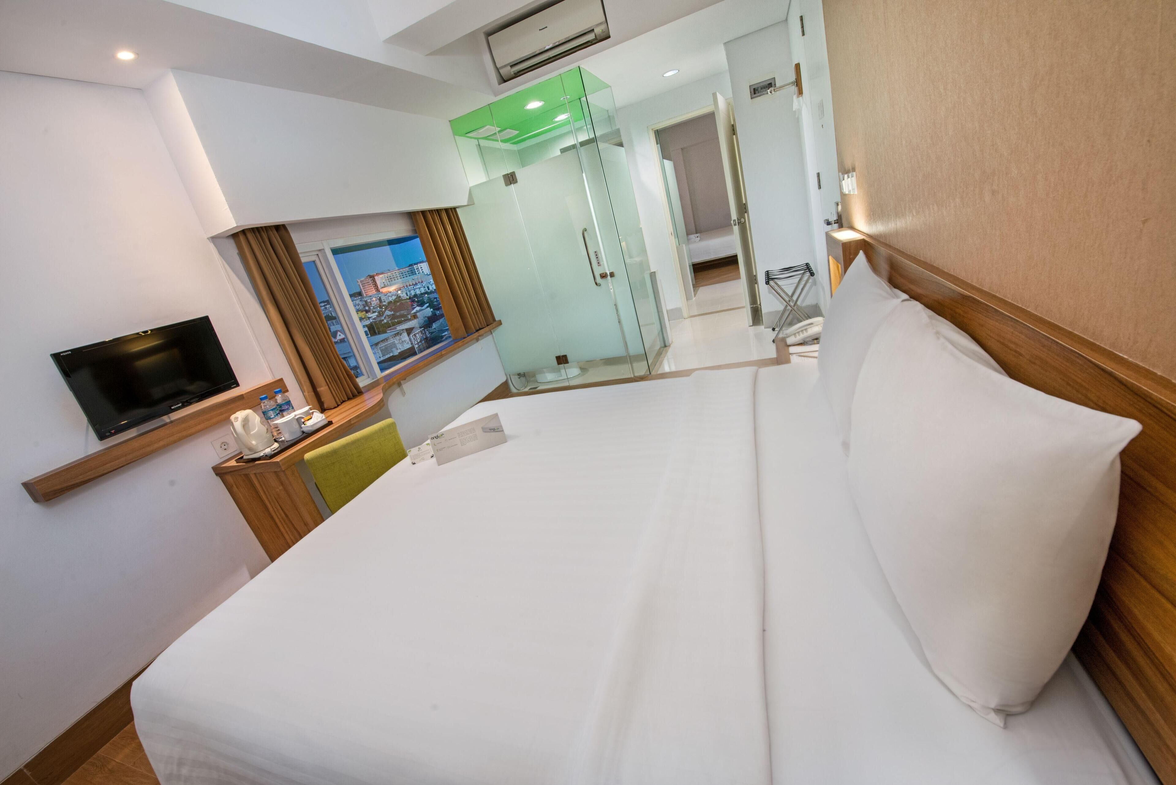 A hotel room with a large bed, a flat-screen TV, a desk with a telephone, and a window with a city view.
