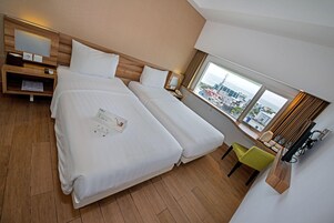 Habitación de hotel con dos camas, una mesita de noche de madera, un escritorio con una silla y un ventanal con vistas a la ciudad.